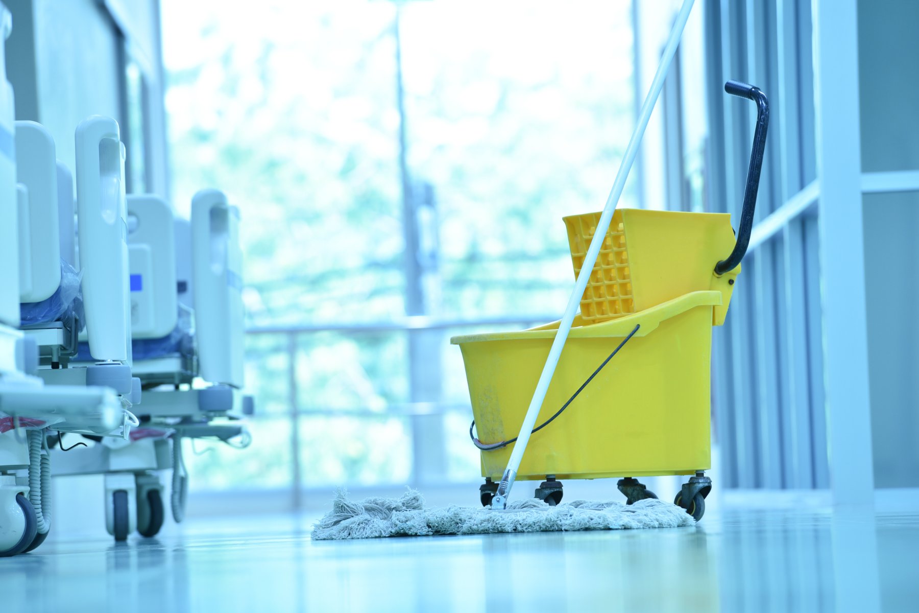 Mop and bucket in a bright, empty clinic corridor beside patient beds